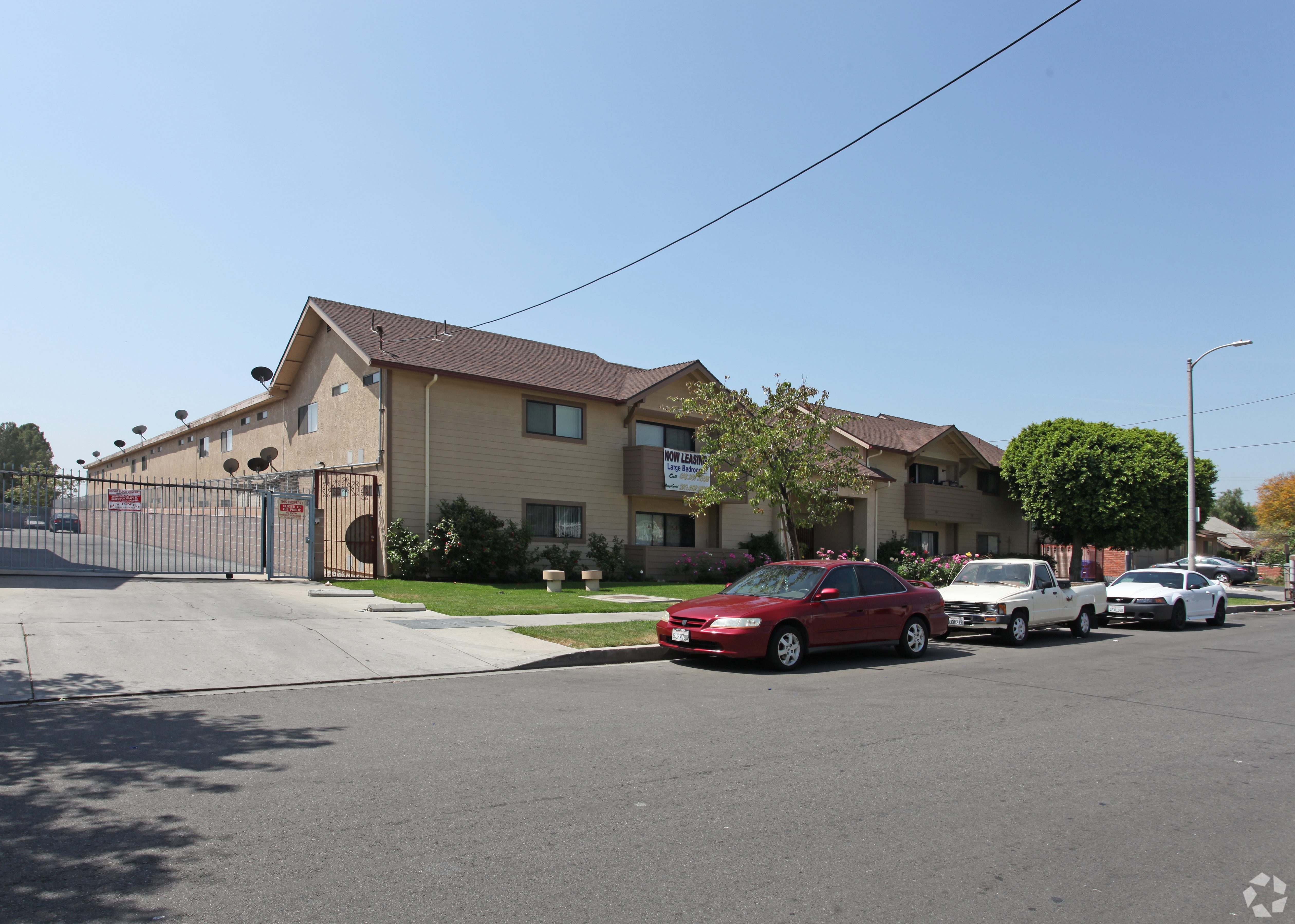 A red car is parked in front of a house with a fence.